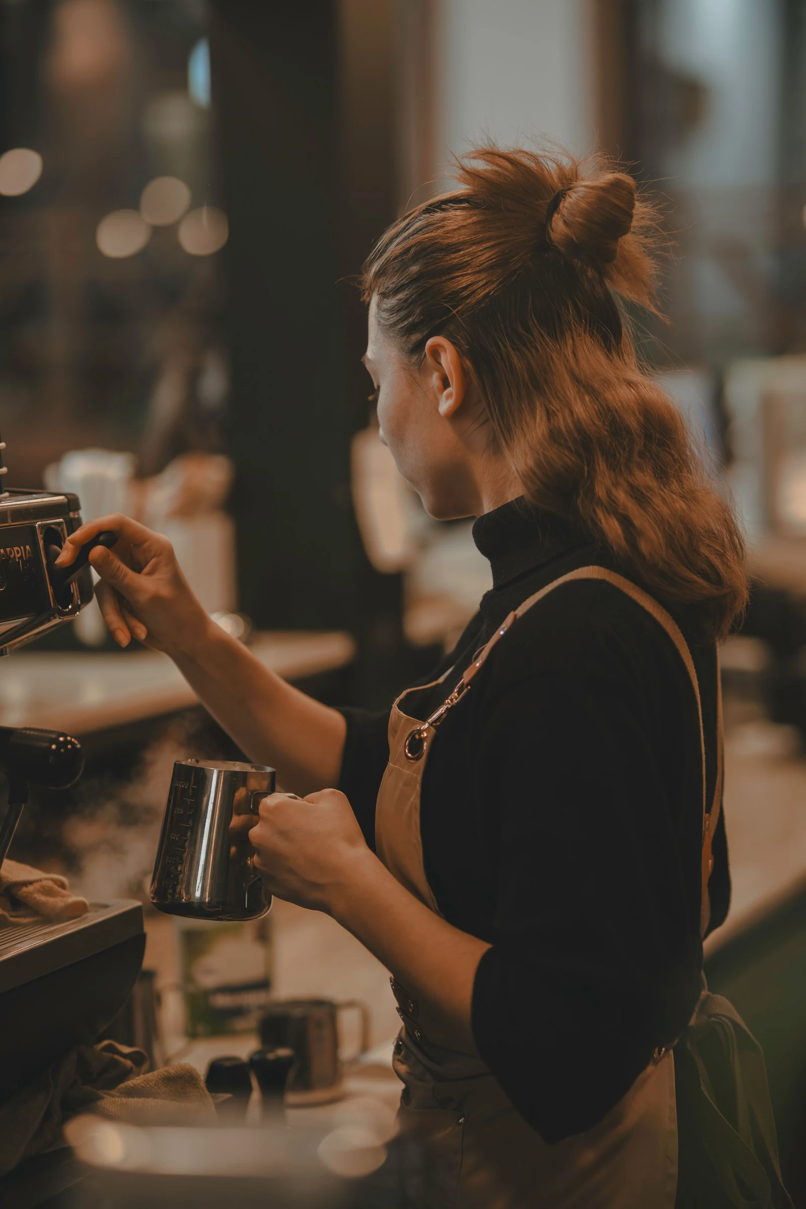 Una barista in grembiule color cuoio prepara il latte alla macchina del caffè.