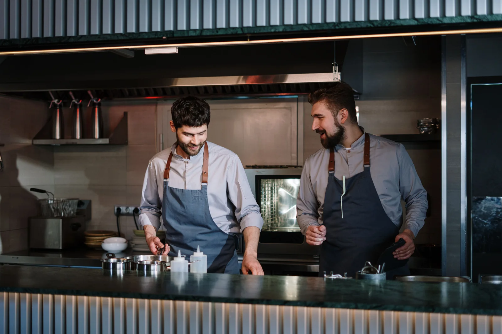 Due cuochi sorridenti in grembiule lavorano insieme al banco di una cucina.