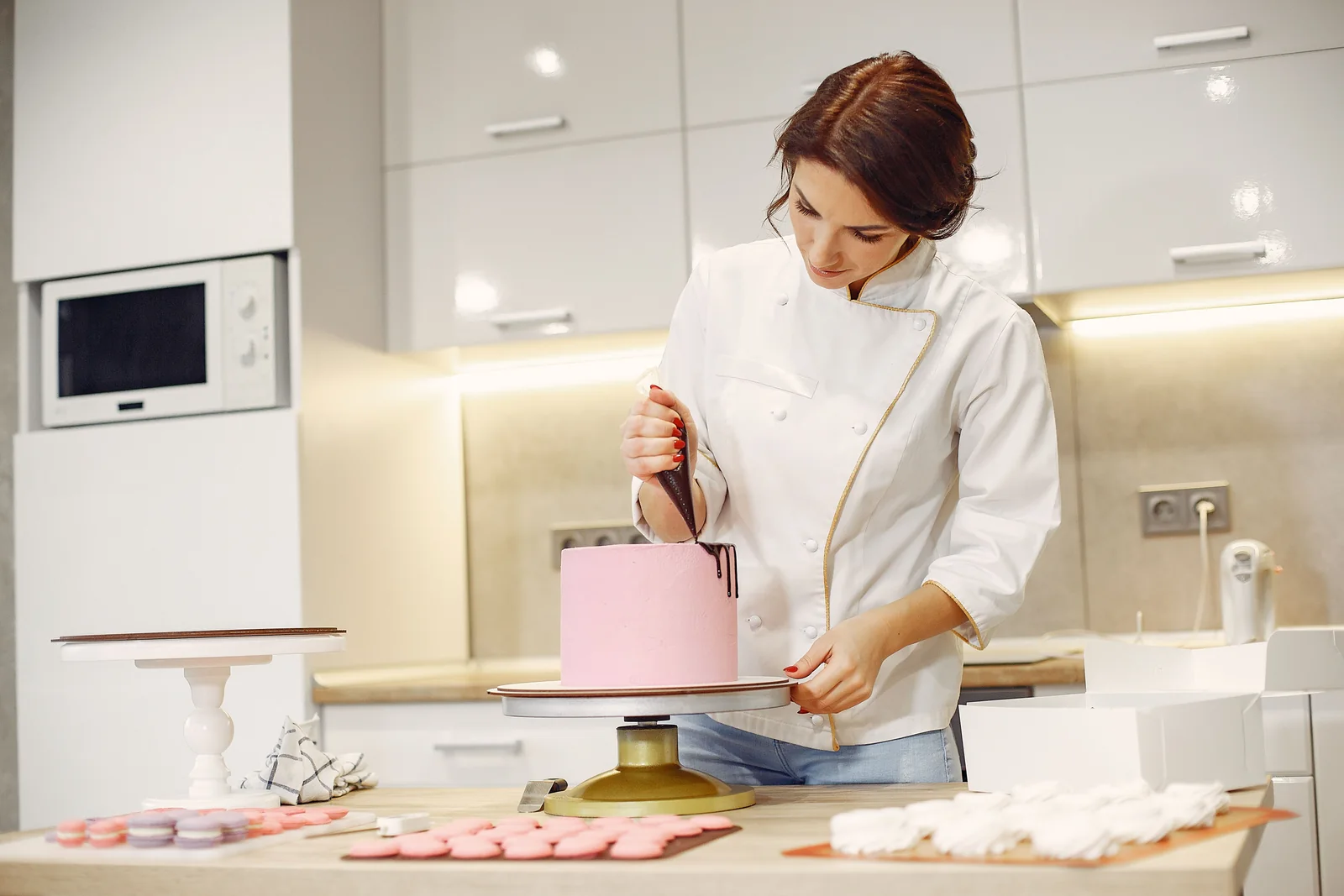 Pasticcera in giacca bianca decora una torta rosa con una sac à poche.