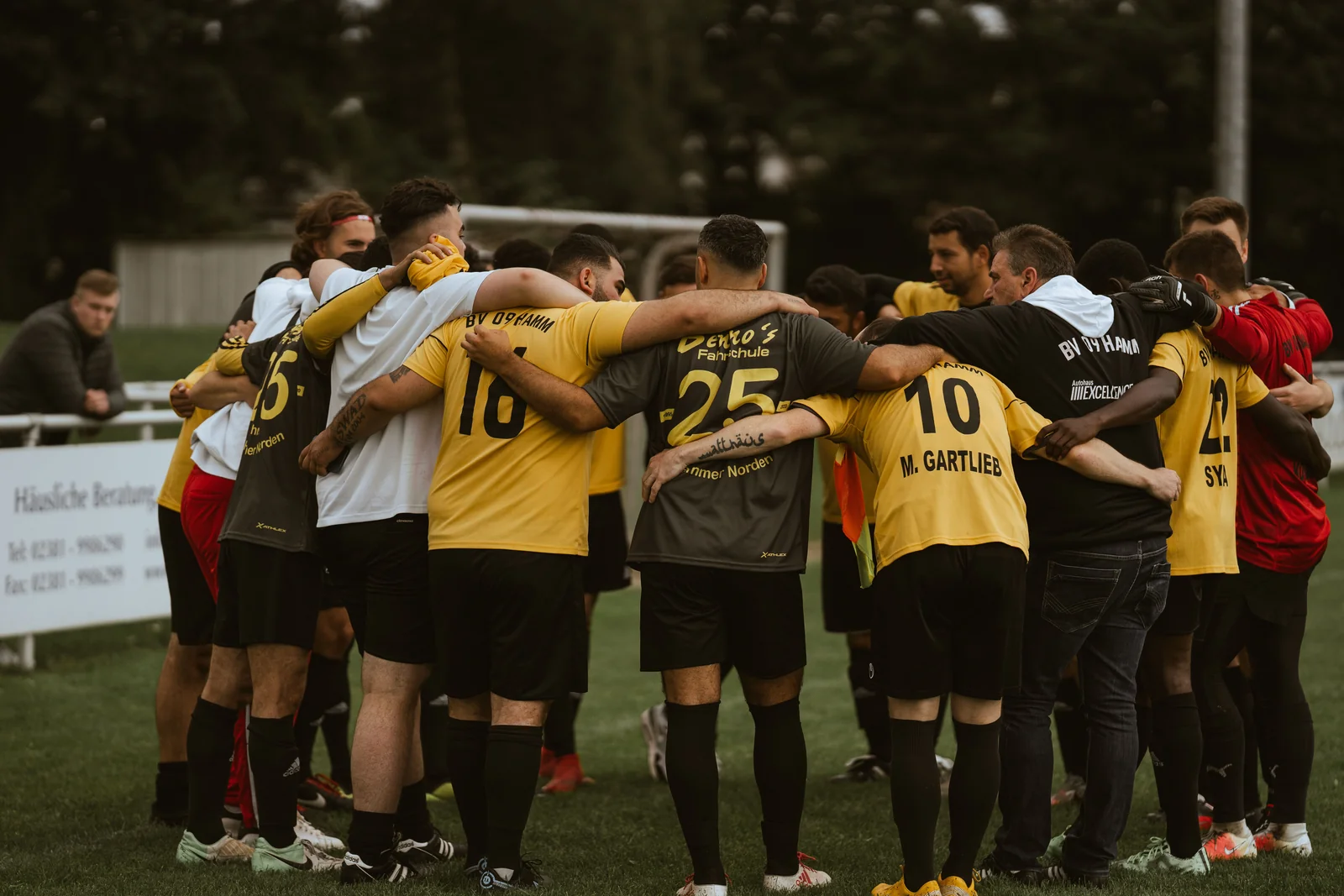 Una squadra di calcio amatoriale si stringe in cerchio sul campo, con divise gialle e nere.